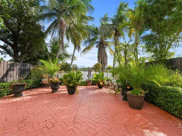 Herringbone-patterned brick patio featuring a perimeter of sculpted hedging, mature palm trees, and decorative metal perimeter fencing