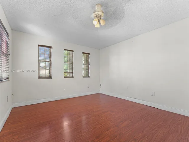 Wood-finish flooring, three vertical windows with horizontal blinds, and a central ceiling-mounted light fixture
