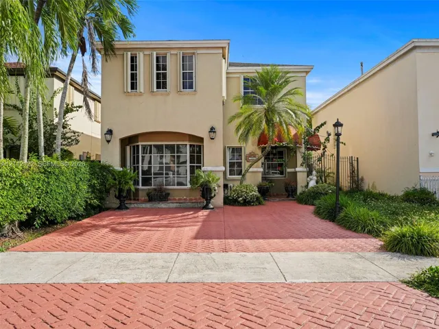 Two-story exterior featuring a stucco façade, herringbone-patterned paved driveway, bay window, and arched entryway with decorative awning