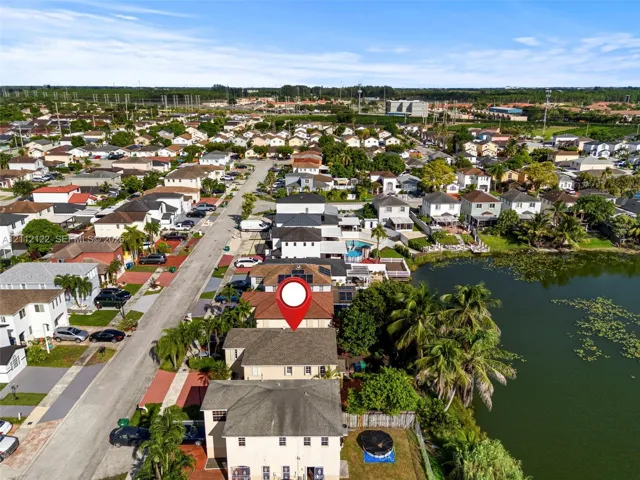 Aerial perspective of a multi-story residence featuring solar panels, a concrete tile roof, and a fenced rear yard bordering a natural lake