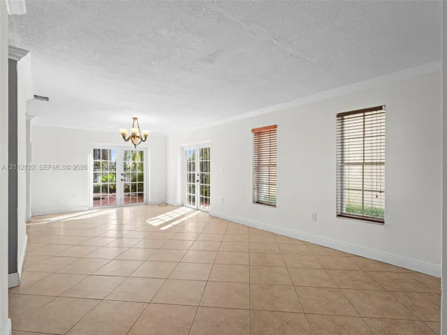Neutral-toned tile flooring, crown molding, two sets of glass-paned French doors, and multi-pane windows featuring horizontal blinds