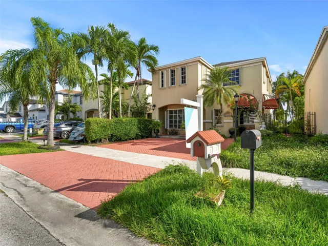 Two-story stucco exterior featuring a red brick-patterned driveway, multi-pane bay window, and custom decorative awnings