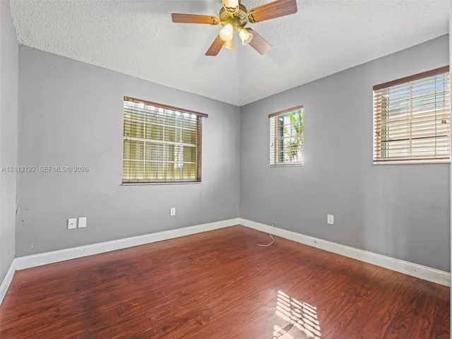 Room featuring wood-finish flooring, vaulted ceilings, a central multi-bulb ceiling fan, and windows equipped with horizontal blinds