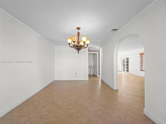 Interior space featuring neutral wall paint, tile flooring, crown molding, an arched passage, and a decorative multi-arm chandelier