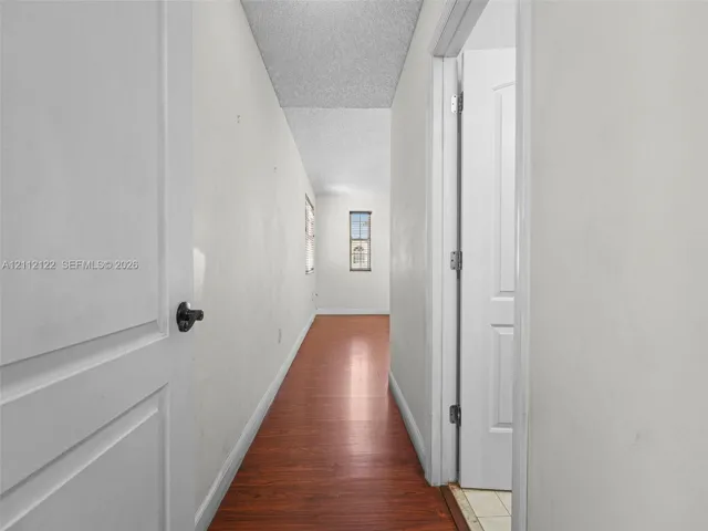 Hallway featuring wood-finish flooring, white walls, and interior paneled doors with matte black hardware