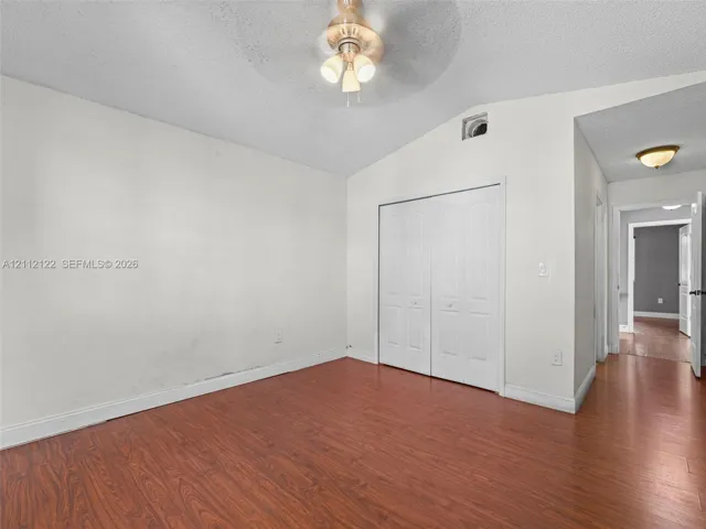 Vaulted ceiling featuring a central multi-bulb ceiling fan, wood-finish flooring, and double-door closet with recessed paneling