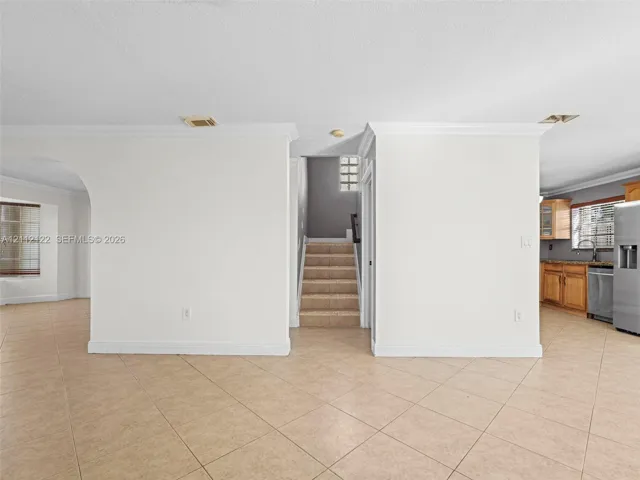 Neutral-toned tile flooring, arched architectural opening, staircase with carpeted treads, and crown molding