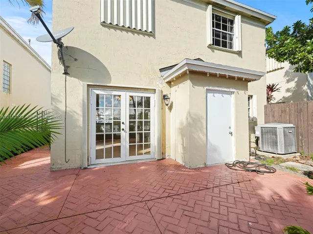 Stucco exterior featuring a red herringbone-patterned paved patio, white French doors with glass panes, and a dedicated exterior utility access door