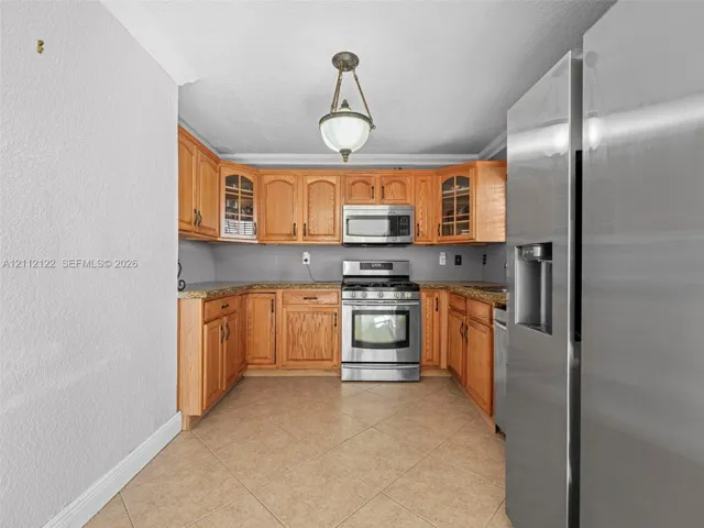 Kitchen featuring wood cabinetry, stone-surface countertops, tile flooring, stainless steel appliances, and a central pendant light fixture