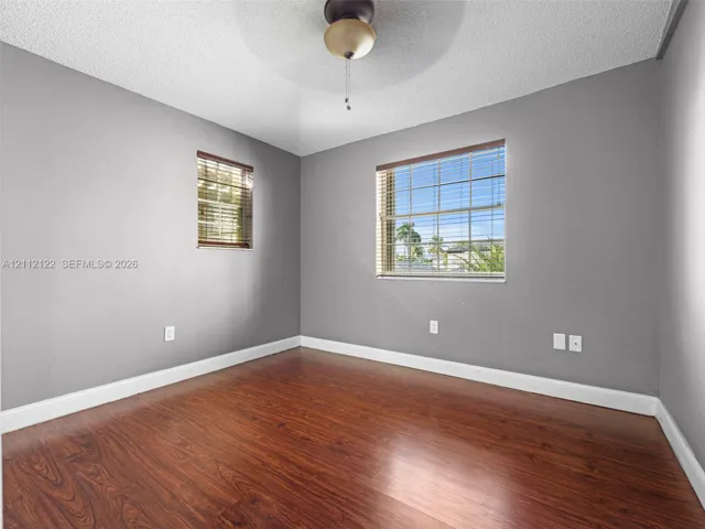 Wood-finish flooring, neutral-toned walls, ceiling-mounted light fixture with fan, and dual windows with horizontal​​‌​​​​‌​​‌‌​‌‌​​​‌‌​‌​‌​‌​​​‌​​ blinds