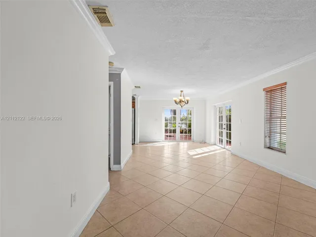 Neutral-toned interior featuring ceramic tile flooring, crown molding, multi-light chandelier, and dual sets of glass-paned French doors