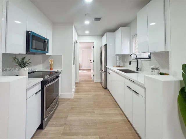 Kitchen featuring high-gloss white cabinetry, white stone-finish countertops, stainless steel appliances, wood-finish flooring, and a matte black gooseneck faucet