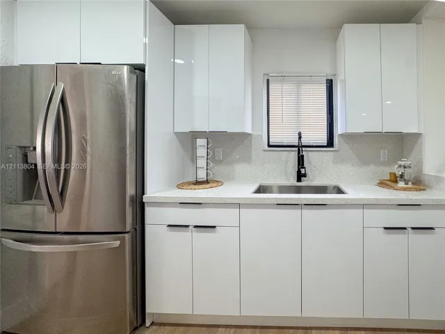 Kitchen featuring white high-gloss cabinetry, stainless steel French door refrigerator, light-toned solid surface countertops, undermount sink, and matte black high-arch faucet