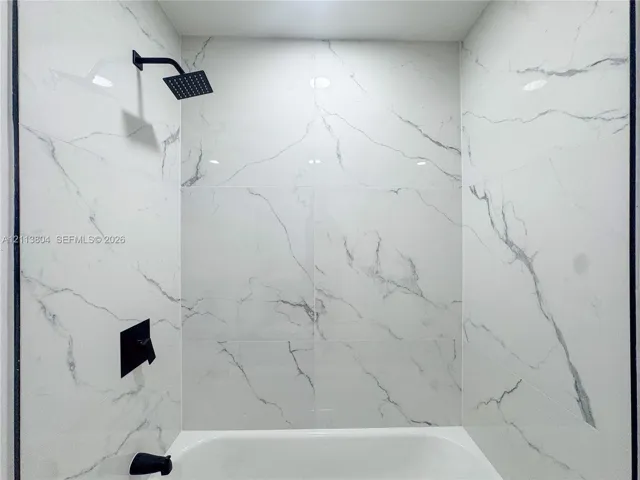Shower area featuring large-format, veined tile wall surround, matte black rainfall showerhead, and matte black wall-mounted faucet controls