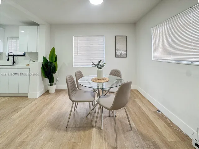 Bright interior space featuring wood-finish flooring, white cabinetry, integrated matte black fixtures, and multiple windows with horizontal blinds