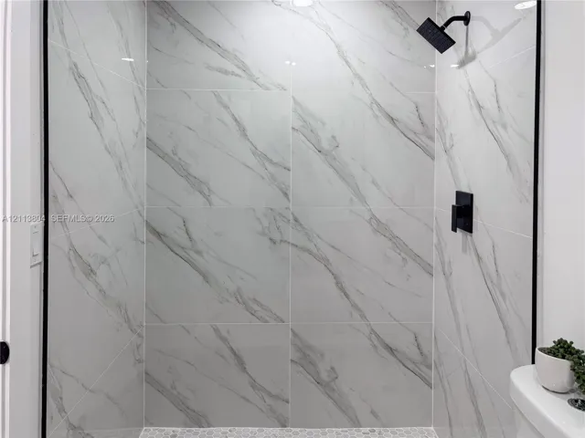 Shower featuring floor-to-ceiling large-format tile with decorative veining, matte black wall-mounted shower head, matte black single-handle mixing valve, and stone hexagon mosaic floor tile