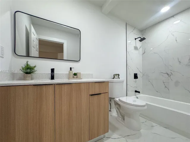 Wood-finish cabinetry with a light-tone countertop, rectangular mirror with matte black framing, and tub-shower combination featuring large-format wall tiling and matte black hardware