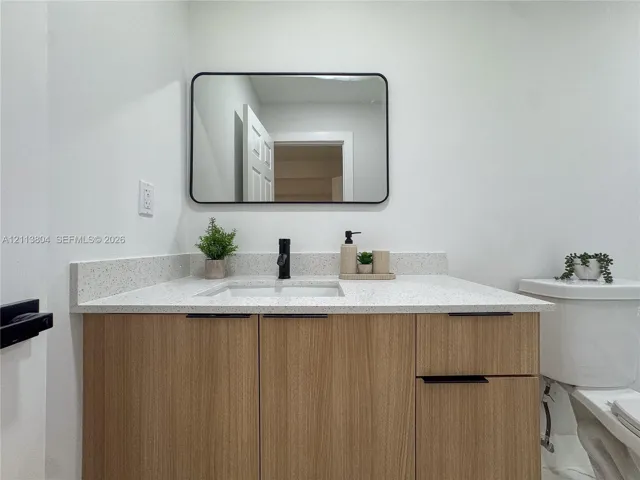 Wood-finish cabinetry featuring black hardware, quartz-composite countertop, undermount sink, matte black faucet, and rectangular black-framed vanity mirror