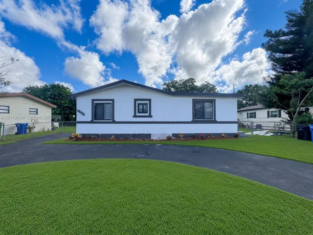 Single-story exterior featuring white stucco finish, contrasting dark trim, manicured lawn, and asphalt driveway