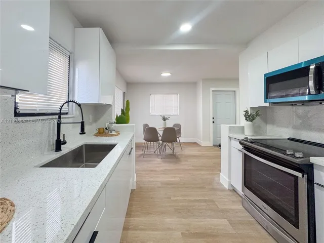 Kitchen featuring white slab cabinetry, light-toned stone-finish countertops, stainless steel undermount sink with a matte black faucet, and wood-finish flooring