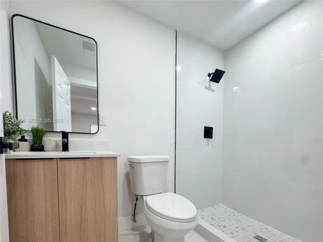 Modern vanity featuring light wood-finish cabinetry, a stone-composite countertop, and a rectangular mirror with a black frame