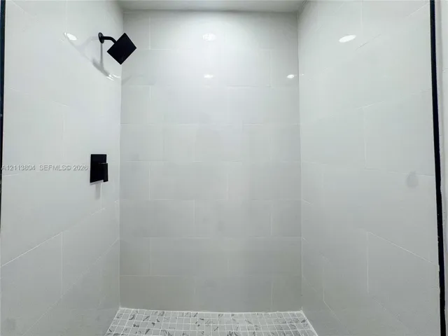 Walk-in shower enclosure featuring white subway tile wall surround, matte black rainfall showerhead, matte black pressure-balance valve, and a mosaic tile floor