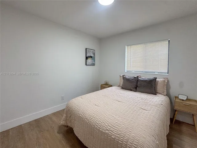 Neutral-toned interior space featuring wood-finish flooring, white walls, and a window with horizontal blinds