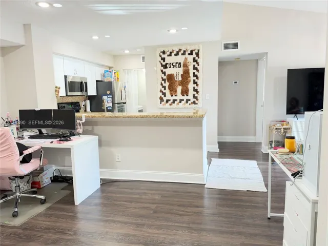 Kitchen featuring white cabinetry, stone-finish countertops, stainless steel microwave, and recessed ceiling lighting over wood-finish flooring