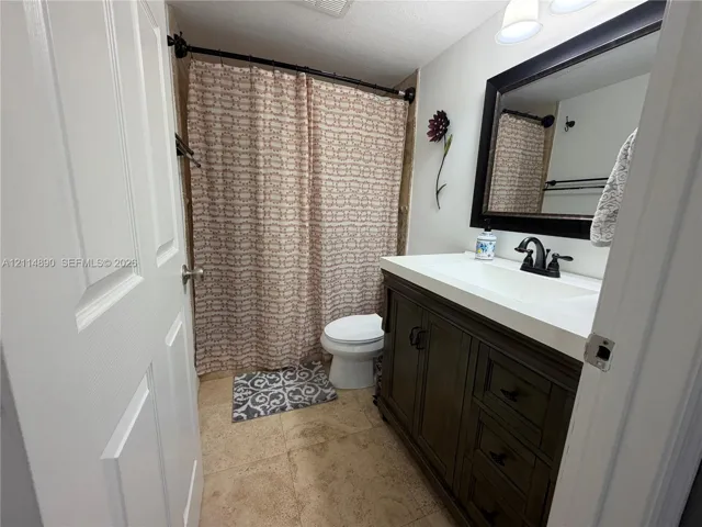 Bathroom featuring a vanity with dark wood-finish cabinetry, a white countertop with an integrated sink, a dark-framed mirror, and a curved shower rod