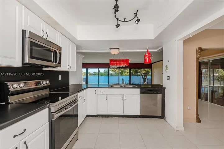 Kitchen featuring white cabinetry, stainless steel appliances, solid-surface countertops, tile flooring, and track lighting