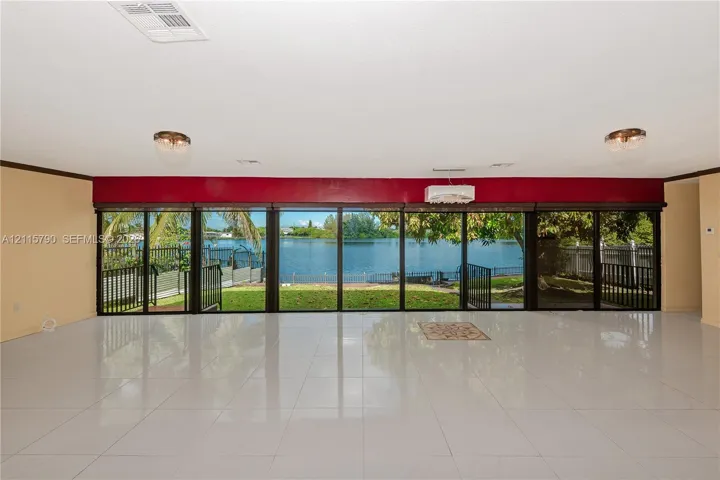 Expansive living area featuring large-format tile flooring, recessed lighting, and an expansive wall of floor-to-ceiling glass sliding doors with water frontage