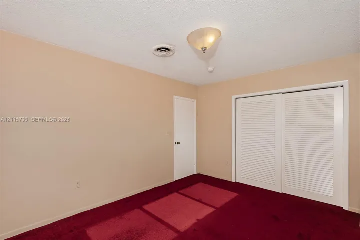 Room featuring red wall-to-wall carpeting, dual-panel louvered closet doors, and a semi-flush mount ceiling light fixture
