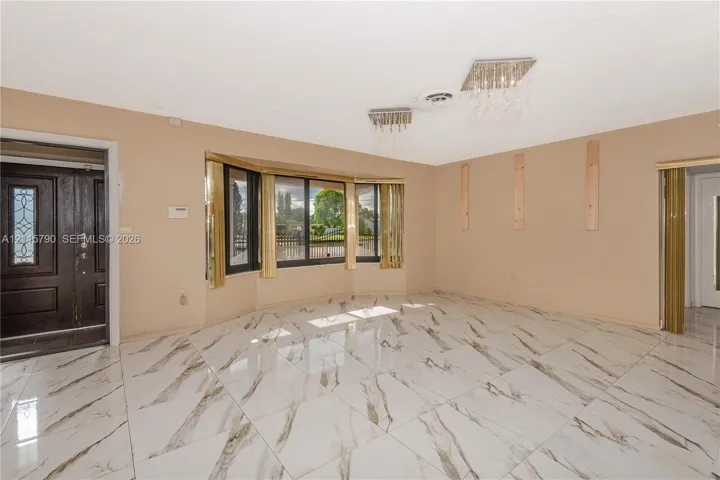 Large-format stone-style tile flooring, expansive bay window, ornate crystal-style ceiling light fixtures, and solid-core dark wood entry door with decorative glass inlay