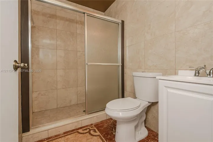 Walk-in shower with sliding glass enclosure and tiled surround, white vanity, and toilet