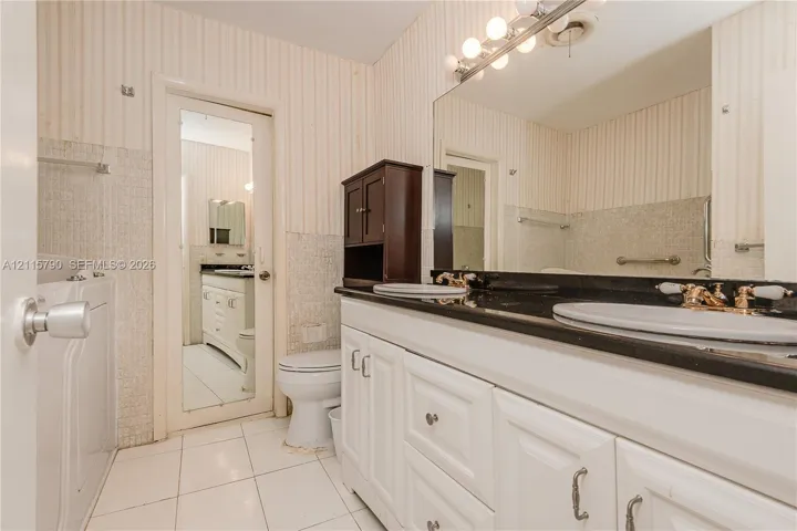 Double vanity featuring white cabinetry, a dark countertop, integrated dual sinks, and an expansive wall-mounted mirror