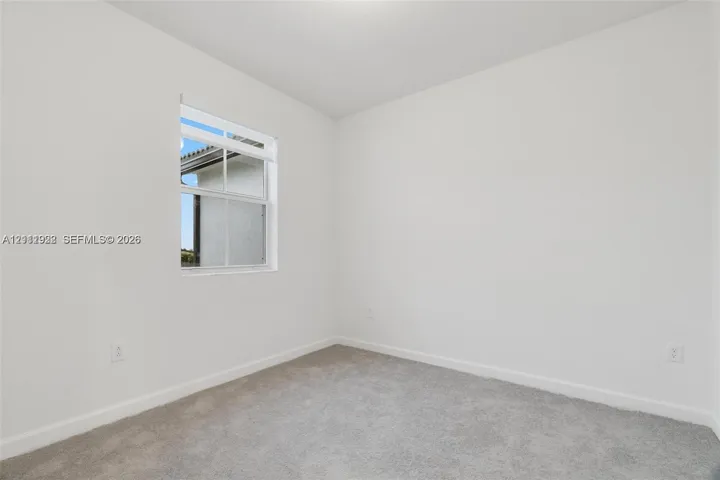 Neutral interior space featuring high-contrast white walls, textured wall-to-wall carpeting, and a single-hung window with a grid pattern