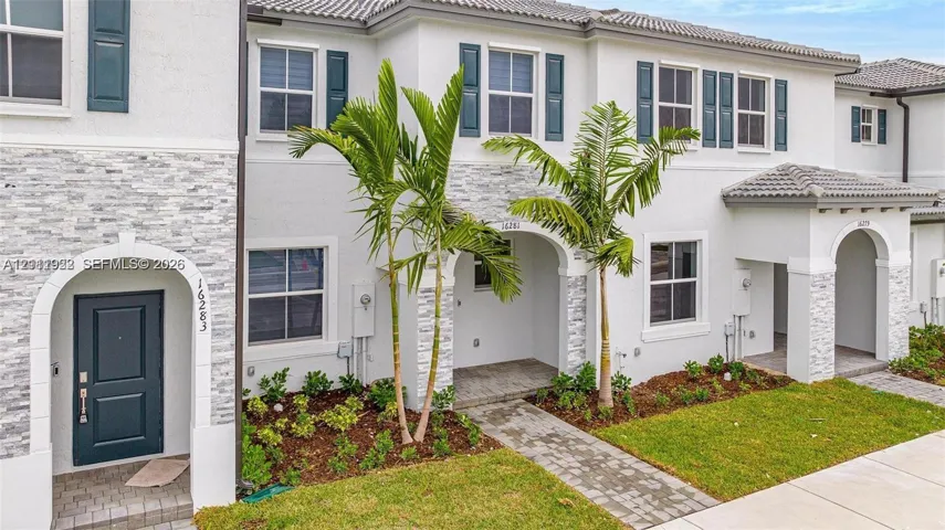Multi-story exterior featuring a light-toned stucco facade, stone veneer accents, arched entryways, and paver walkways