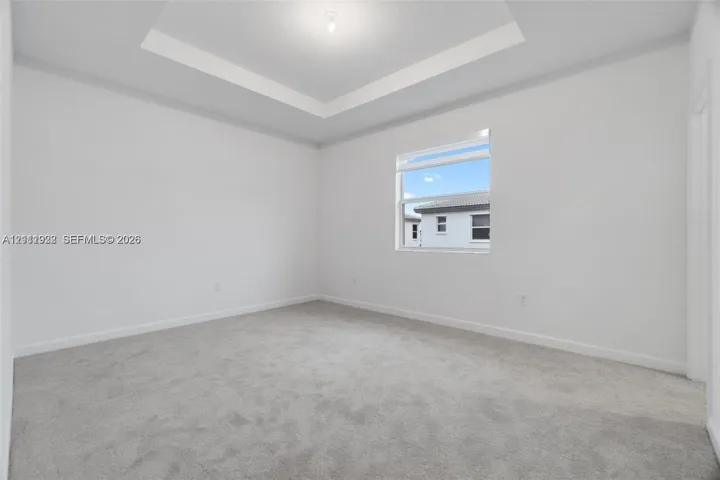 Room featuring a tray ceiling, neutral wall coloring, and wall-to-wall carpeting