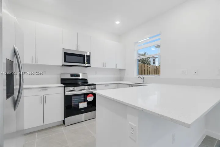 Kitchen featuring white flat-panel cabinetry, quartz countertops, a peninsula breakfast bar, stainless steel appliances, and large-format tile flooring