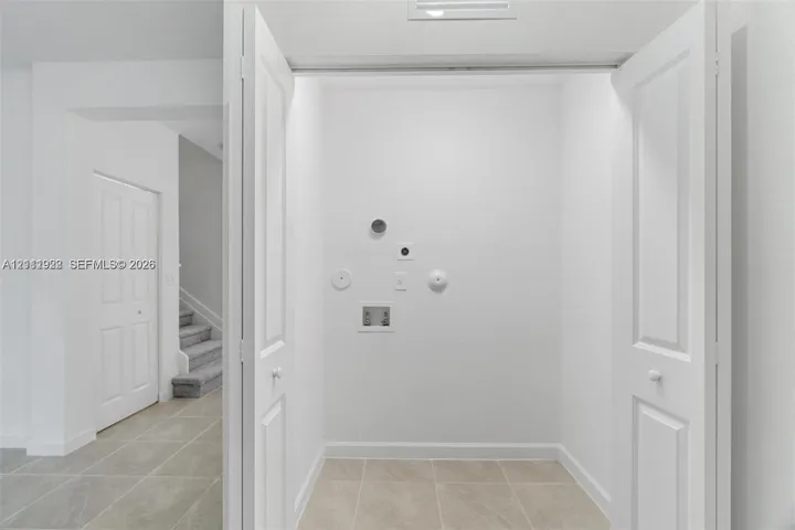 Dedicated utility area featuring bi-fold doors, tile flooring, and integrated plumbing hookups