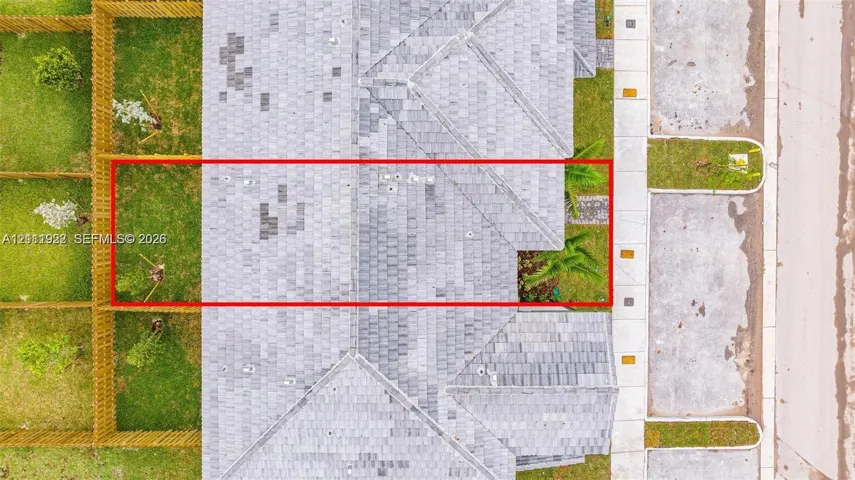 Aerial view featuring an asphalt shingle roof, a fenced perimeter, and a grass-covered outdoor area