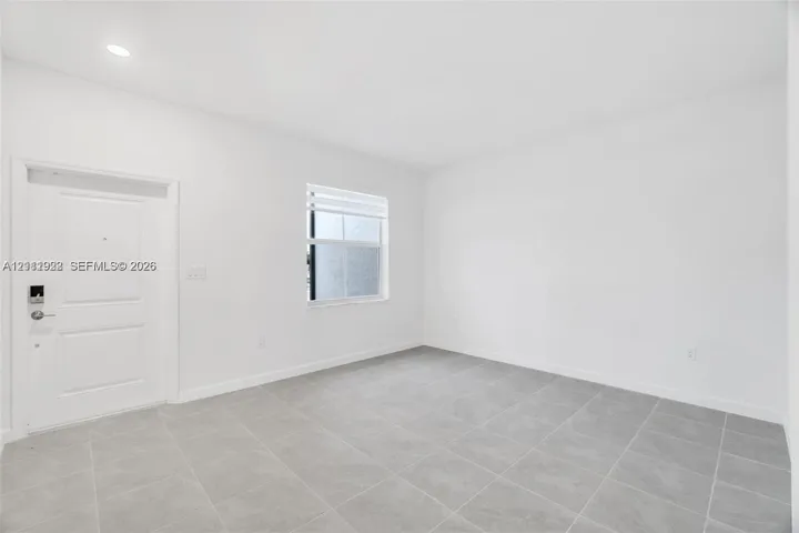 Neutral-toned interior space featuring tile flooring, smooth white walls, recessed ceiling lighting, and a single-panel entry door with integrated electronic lock