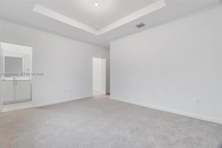 Room featuring a tray ceiling, neutral wall-to-wall carpeting, and a built-in vanity with cabinetry