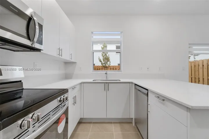 Kitchen featuring flat-panel white cabinetry, stone-surface countertops, stainless steel appliances, and tile flooring