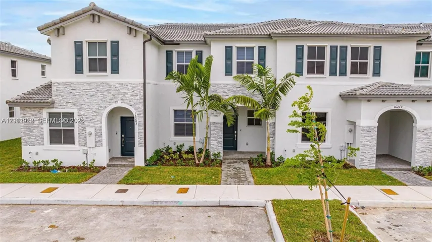 Two-story exterior featuring a light-toned stucco finish, decorative stone veneer accents, multi-pane windows with dark shutters, and arched entryway detailing