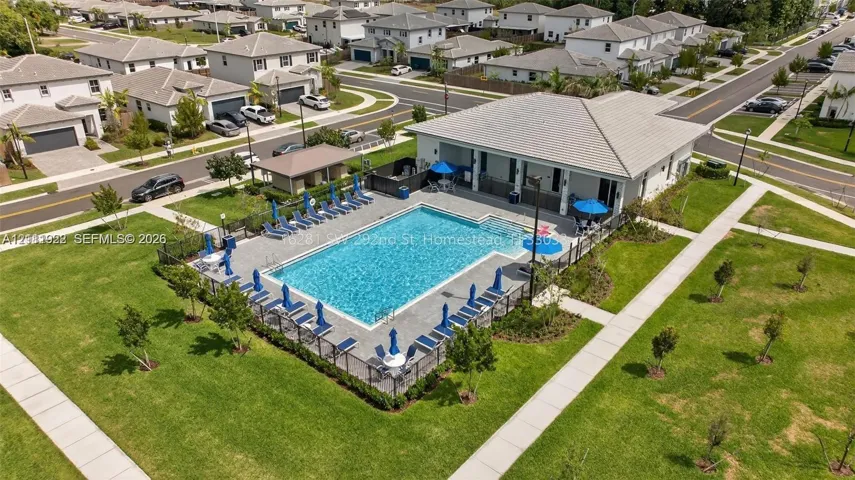 Community recreation center featuring an outdoor swimming pool, concrete pool deck, covered pavilion, and surrounding landscaped grounds
