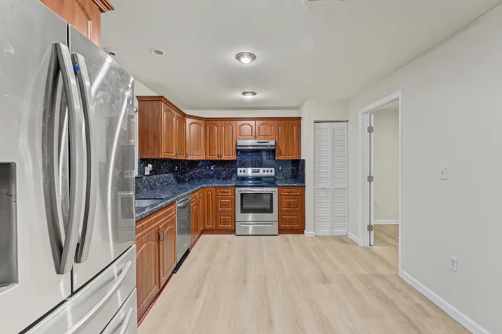 Kitchen featuring wood cabinetry, stone-surface countertops, stainless steel appliances, and wood-finish flooring