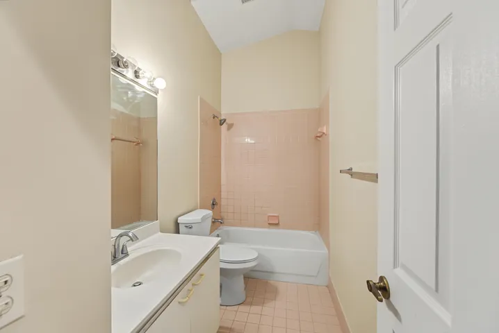 Bathroom featuring a vaulted ceiling, vanity with a white integrated sink, porcelain-tiled tub enclosure, and ceramic-tiled flooring