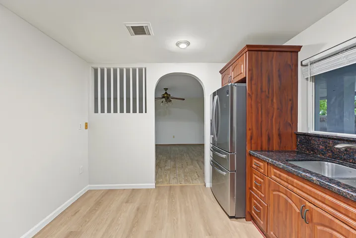 Kitchen featuring wood-finish cabinetry, stainless steel refrigerator, dark stone-style countertops, wood-finish flooring, and an arched entry