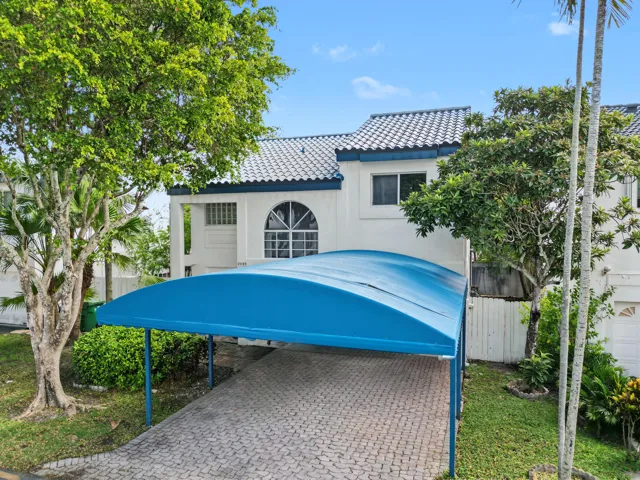 Stucco exterior featuring a tiled roof, arched window, and paved driveway with a covered carport